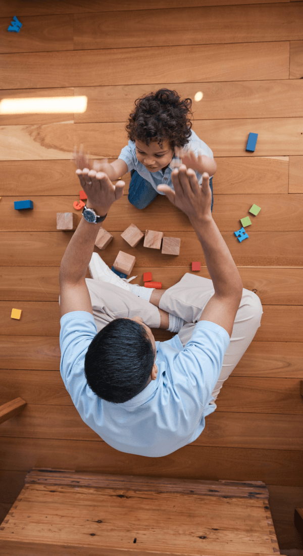 Father and young child playing with educational toys on wooden floor, supporting early learning and development